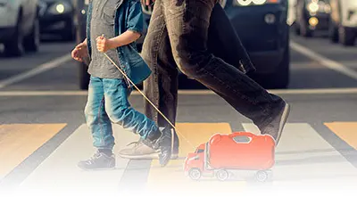 Adult and child crossing street with suitcase.