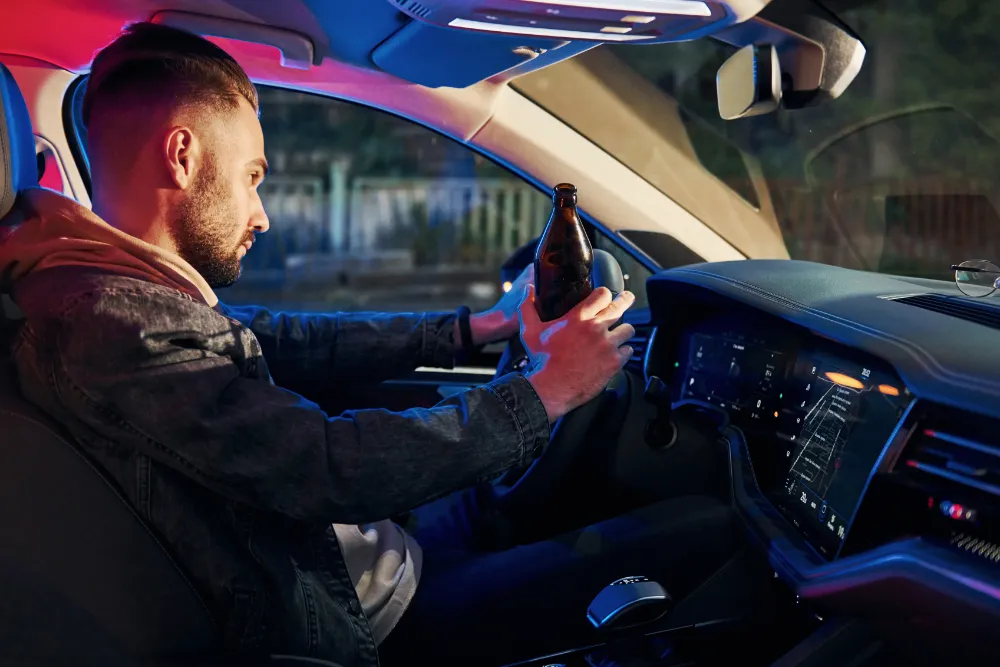 Man holding beer bottle while driving car.