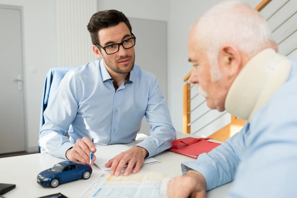 Consultation between man and injured elderly person at desk.